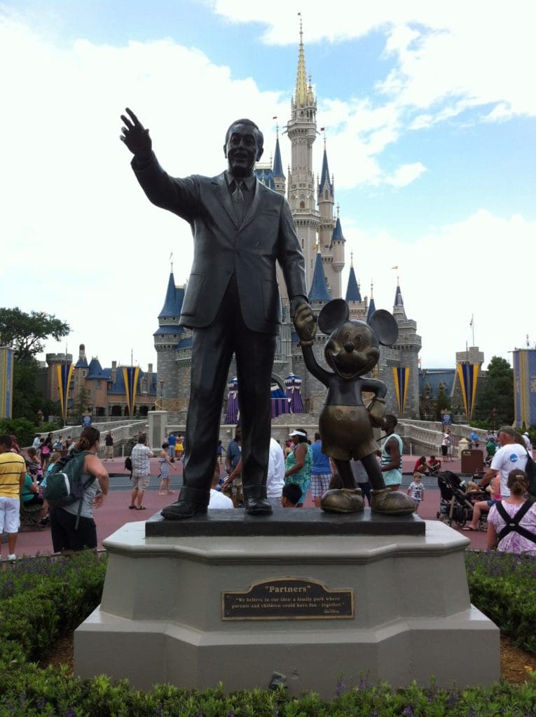 A statue of walt disney and mickey mouse in front of the castle.
