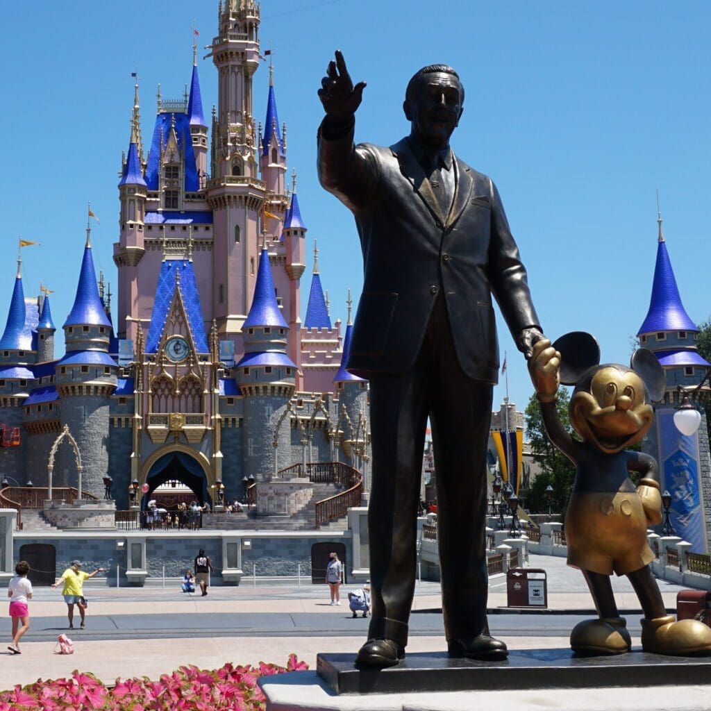 A statue of walt disney and mickey mouse in front of the castle.
